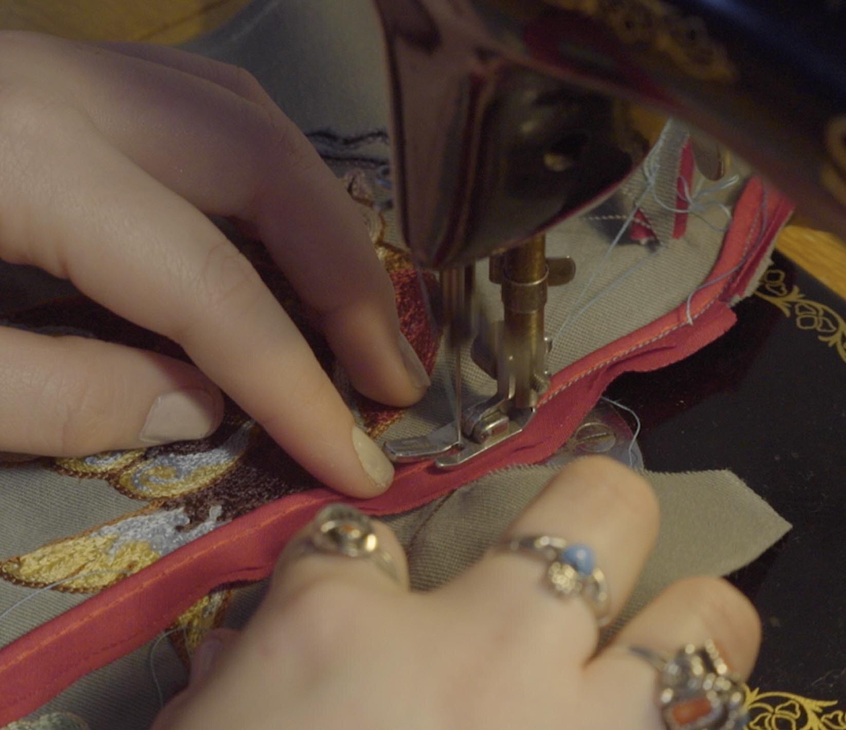 Riley's hands guiding embroidered fabric through a sewing machine