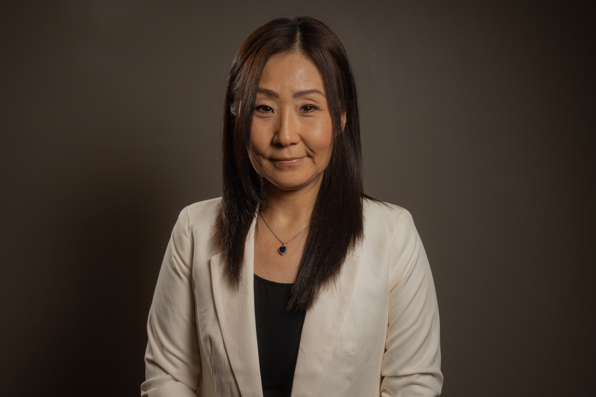 Woman in a light blazer against a dark studio background