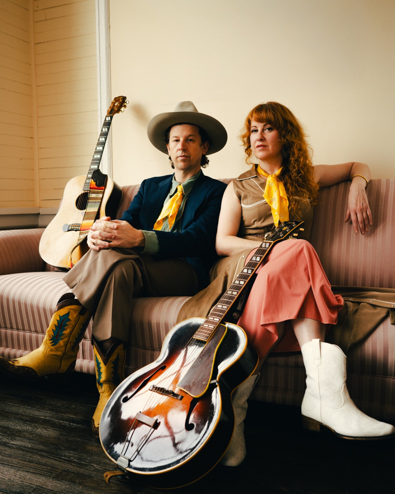 A western-styled couple seated together on a couch with their instruments