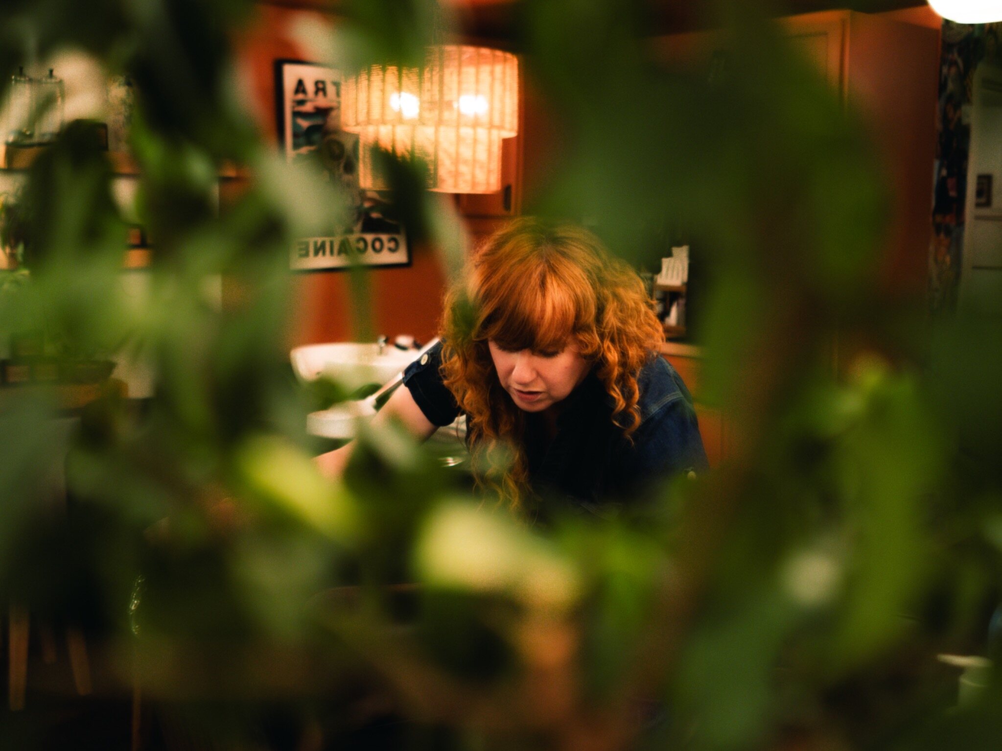 A stylist working through layers of plants and warm salon light